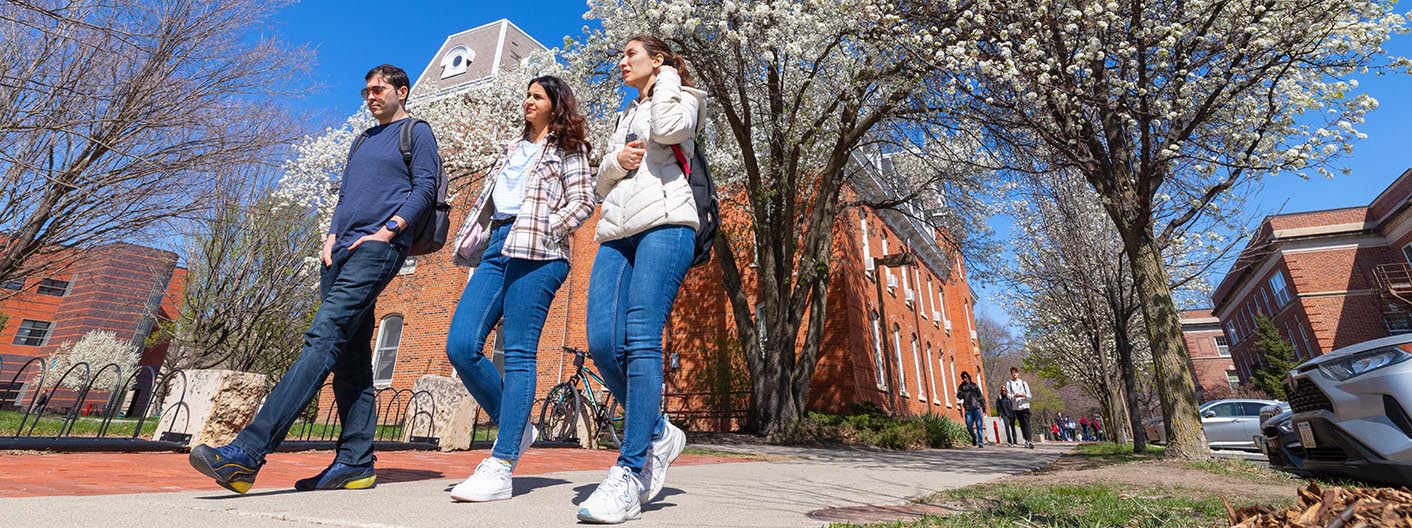 Three students walk on campus in the early spring.